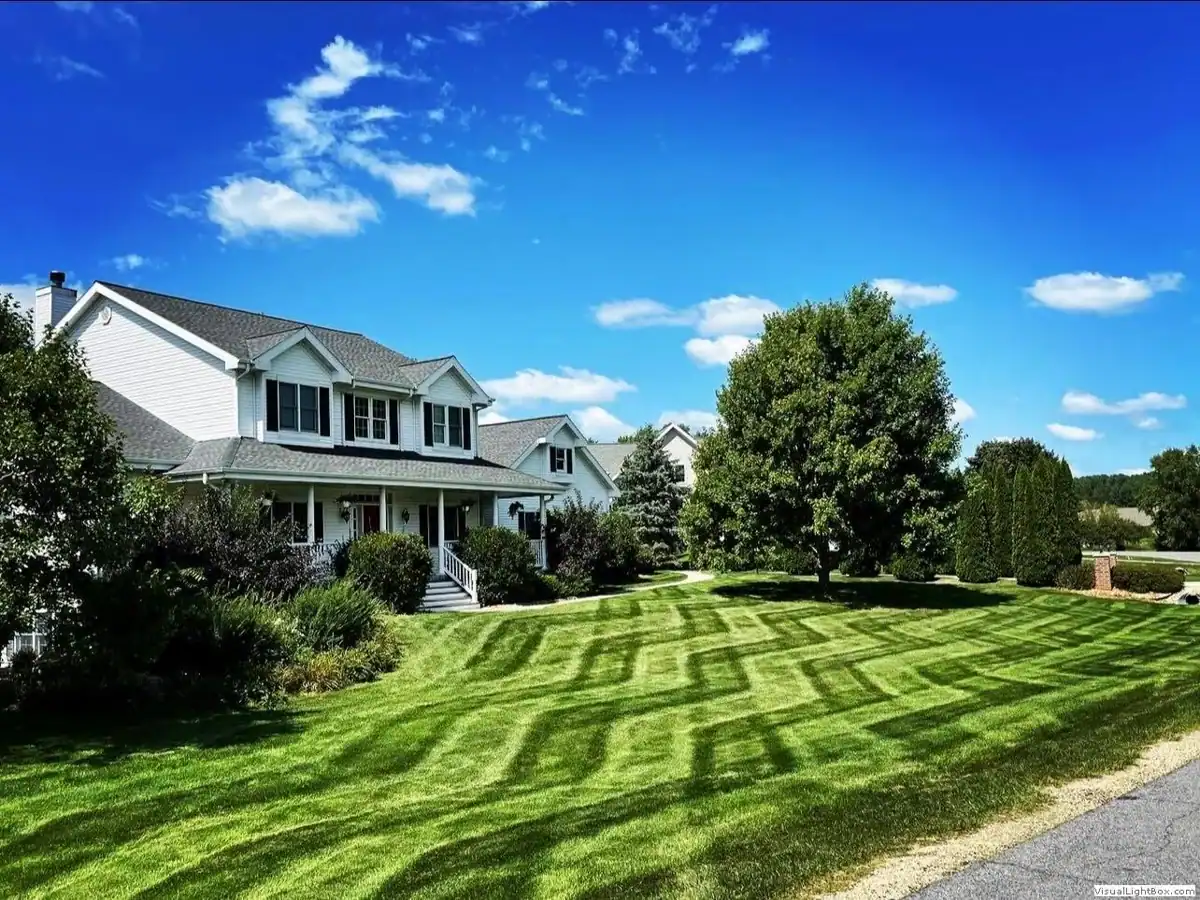 Beautiful well-maintained lawn with suburban house and trees under blue sky.